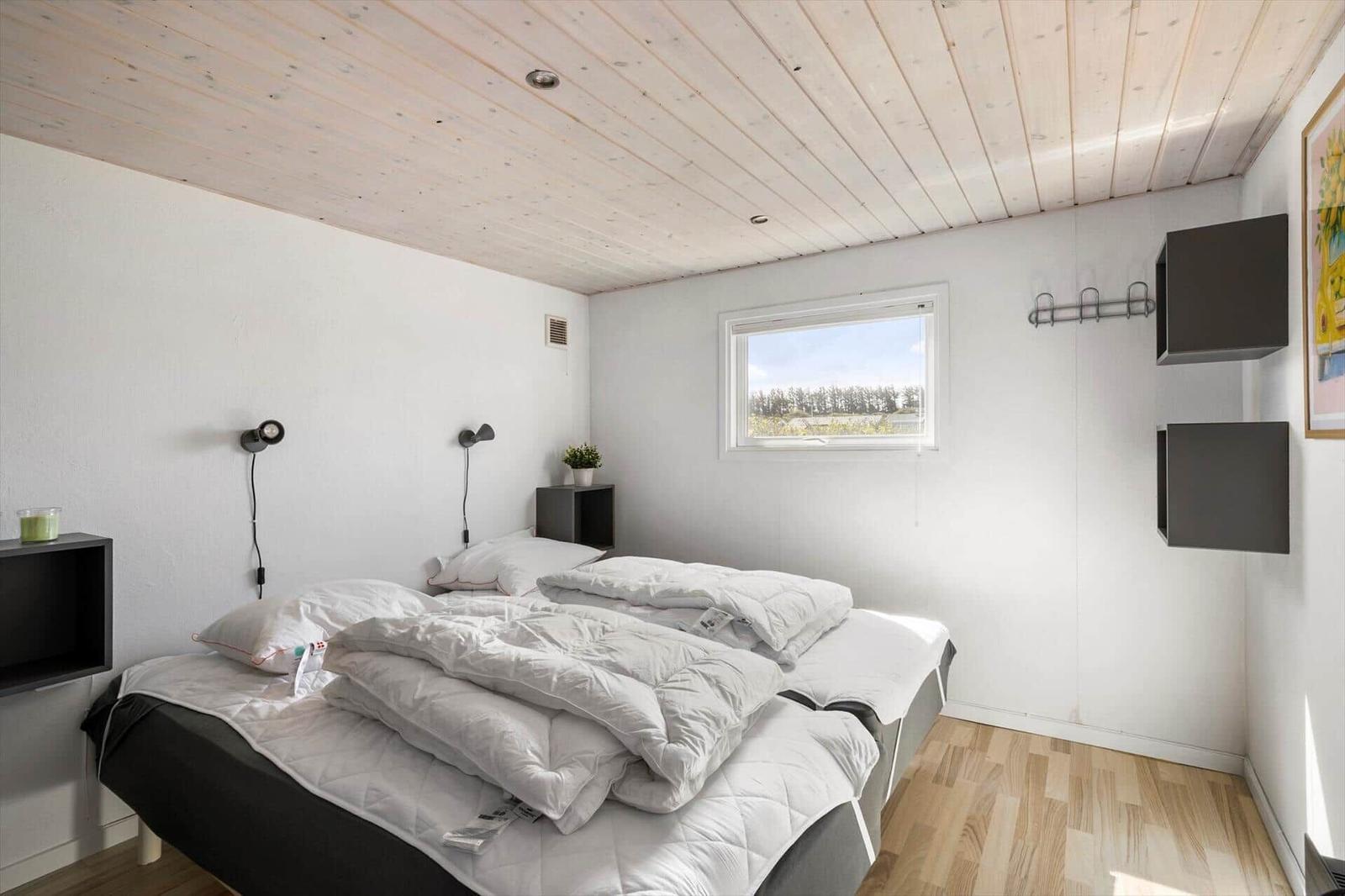 Bedroom with double bed, wooden floor, and window. Ceiling made of wood, wall shelves, and nightstands.