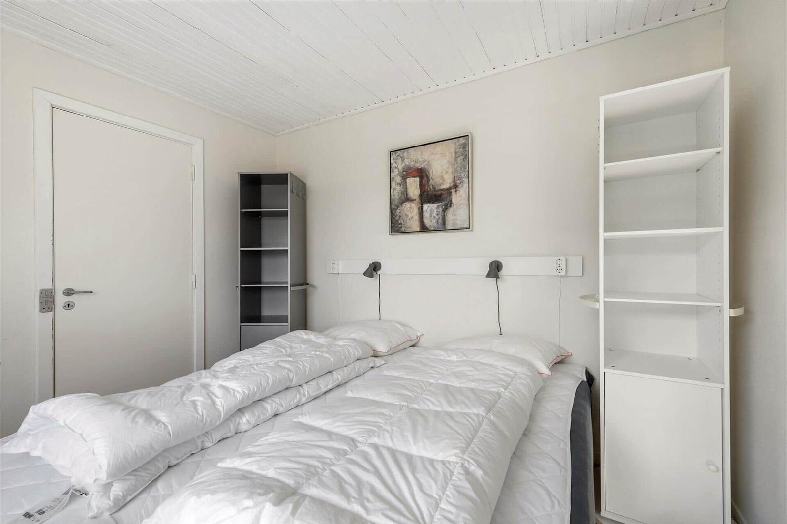 Bedroom with bed, white shelves, and wall art. Ceiling with wooden planks.