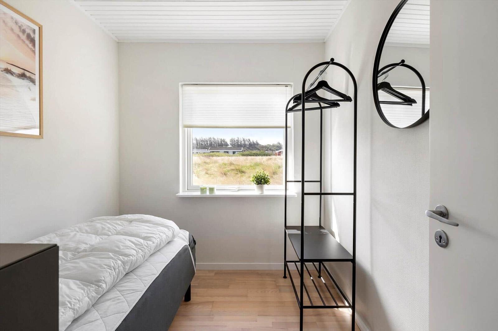 Bedroom with bed, clothing rack, and window overlooking green area.