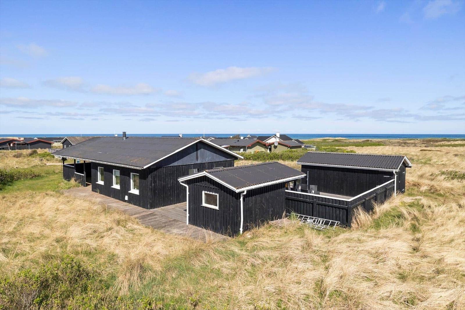 Black wooden houses on dunes with sea view and wooden terrace.