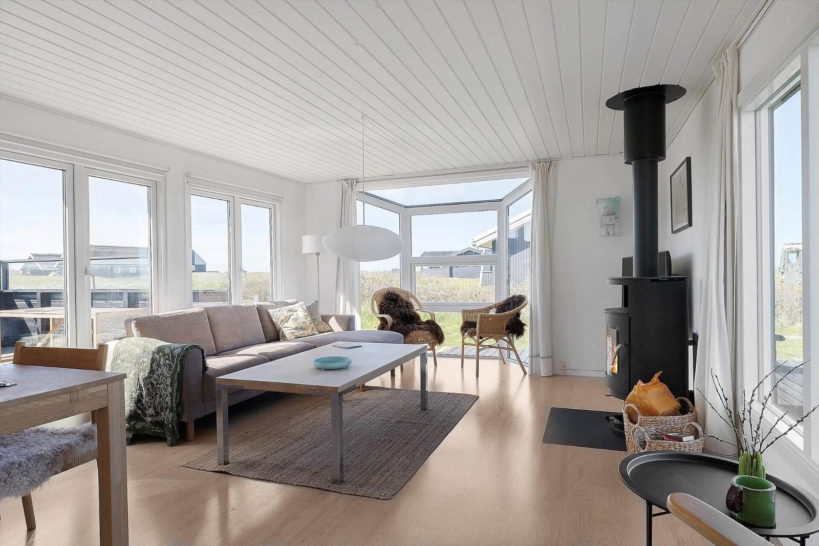 Wohnraum mit Sofa, Kamin und großen Fenstern. Holzboden und weiße Wände.