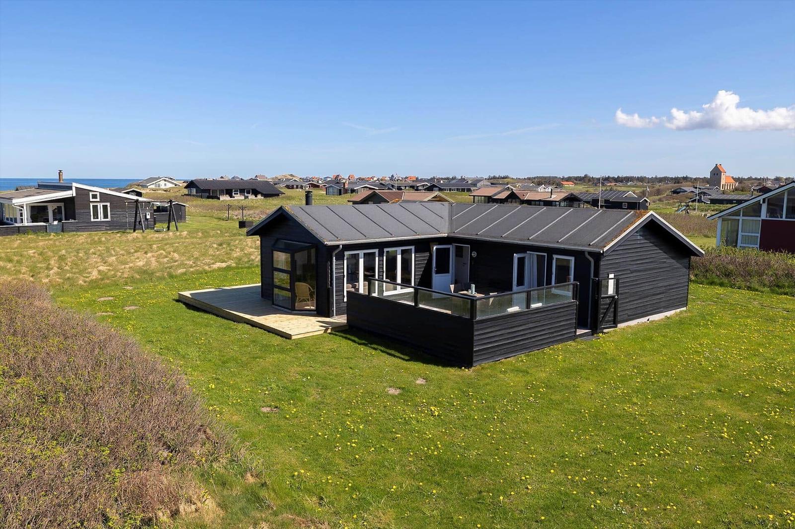 Schwarzes Ferienhaus mit Terrasse auf grünem Grundstück. Blick auf Küstenlandschaft.