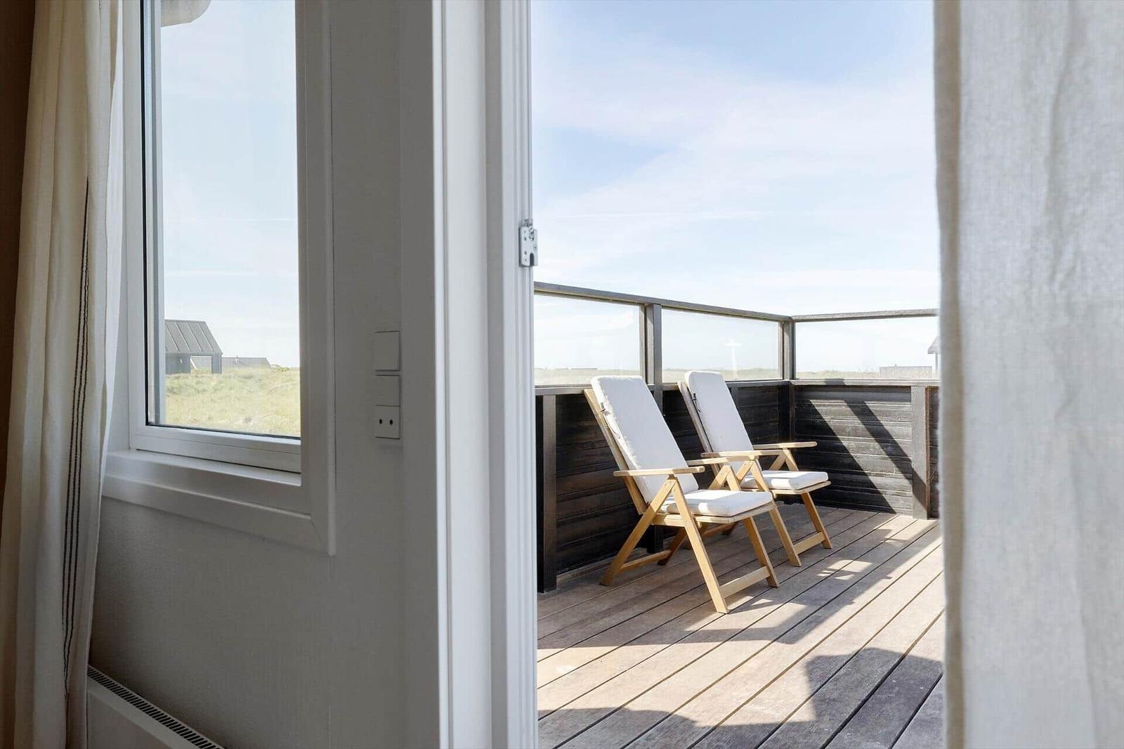 Terrasse mit zwei weißen Liegestühlen und Holzboden. Blick auf Grünflächen und Himmel.