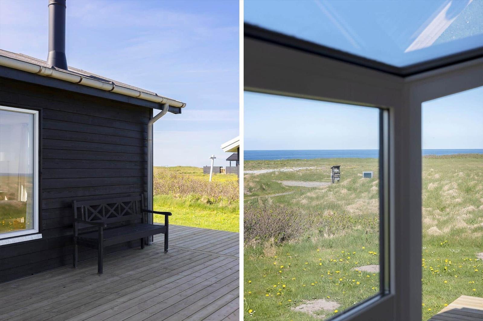 Schwarzes Haus mit Holzterrasse und Blick auf Grasland und Meer.
