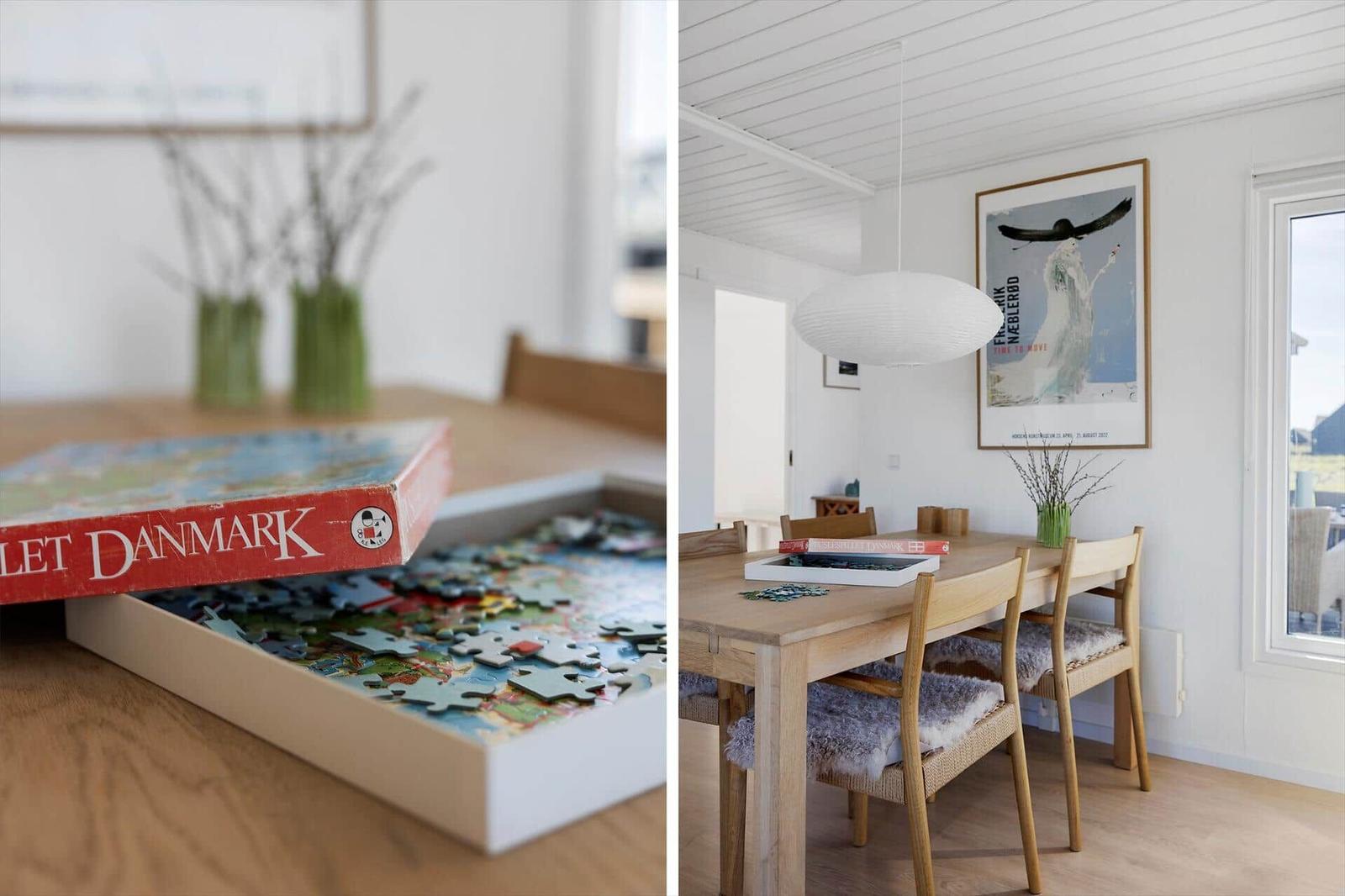 Esszimmer mit Holztisch, Stühlen und Puzzle. Wandbild und Deckenleuchte sichtbar.