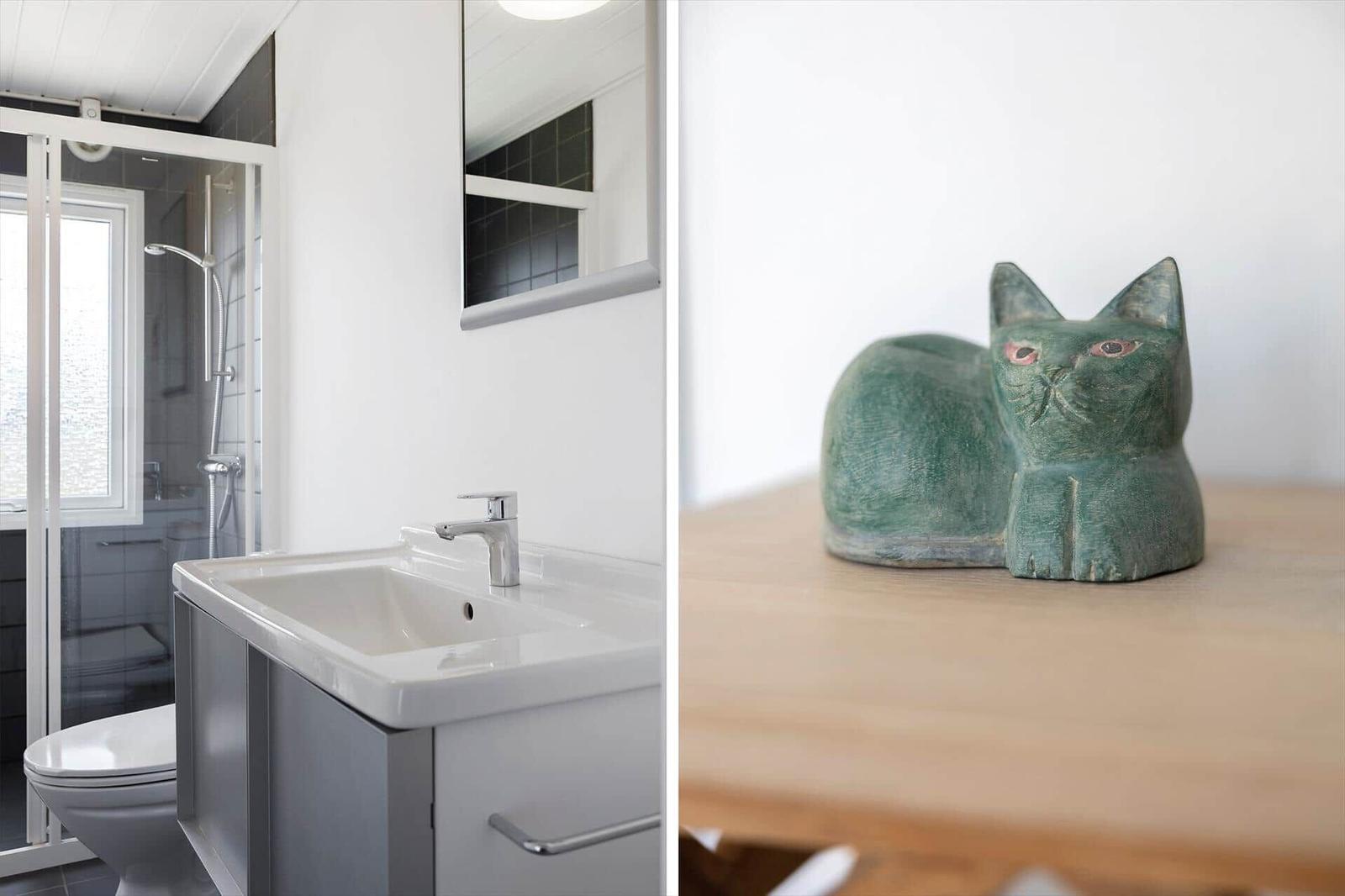 Badezimmer mit Dusche und Waschbecken. Grüne Katzenfigur auf Holztisch.