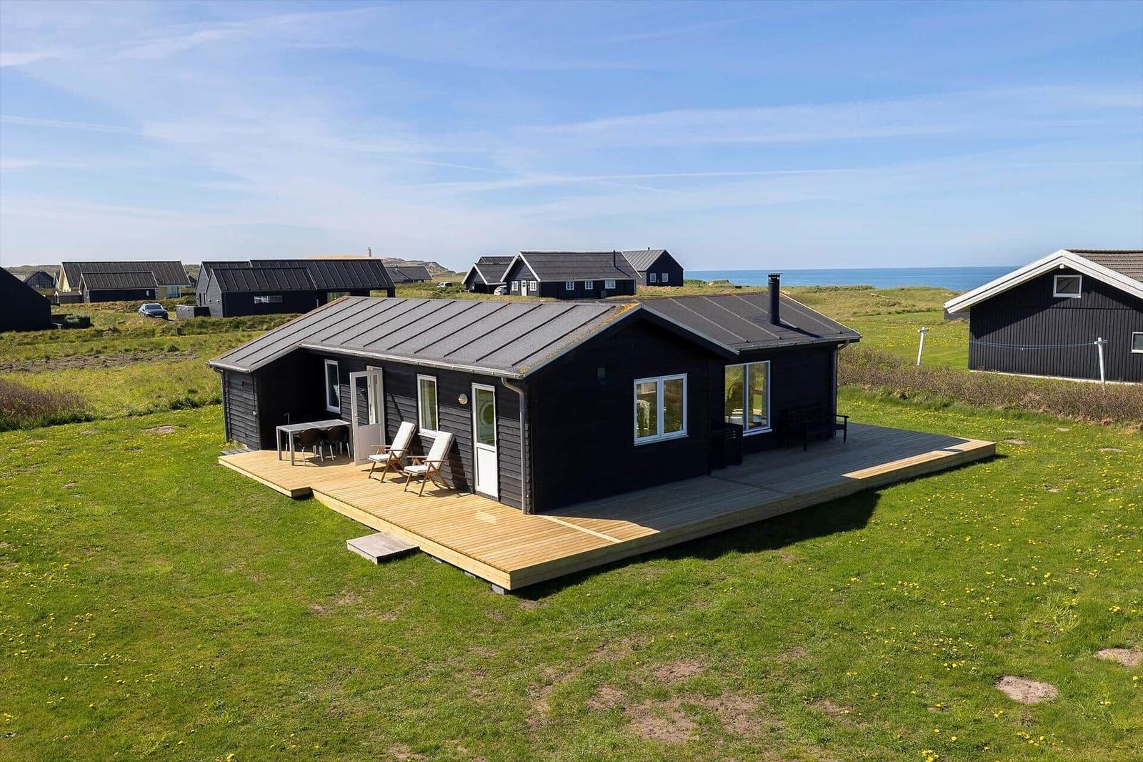 Ein schwarzes Ferienhaus mit Holzterrasse, Garten und Meerblick.