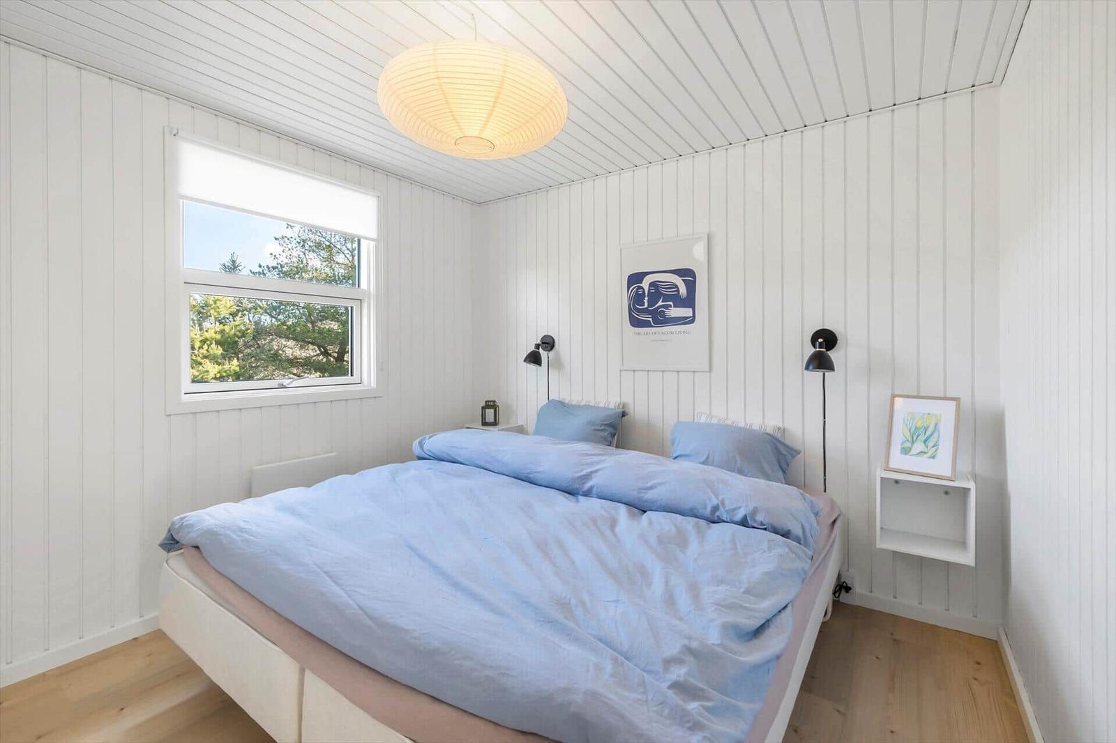 Bedroom with bed, window, and wall paneling. Ceiling lamp and wall lamps.