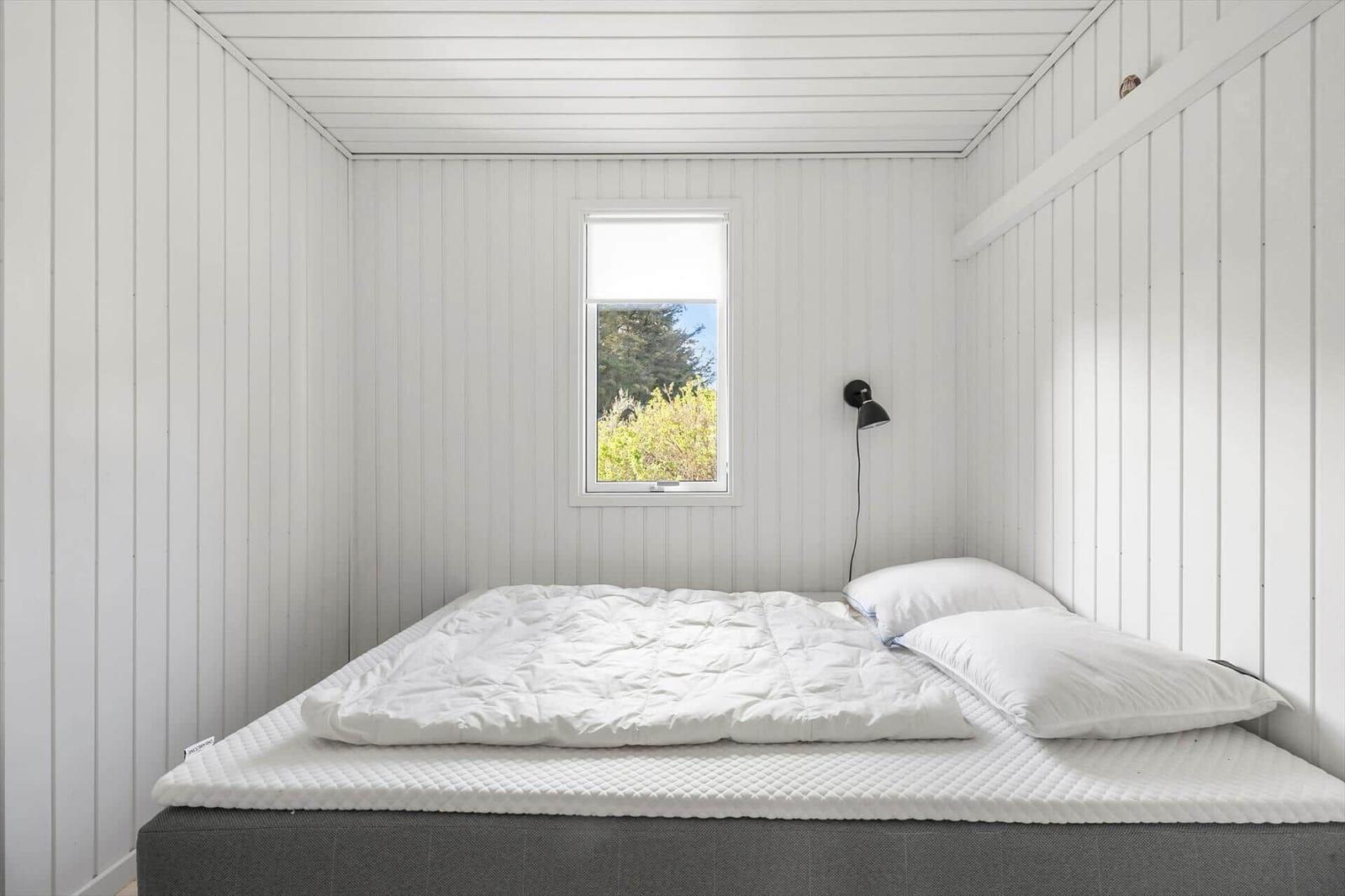 Bedroom with white wood paneling, bed, and window with outdoor view.