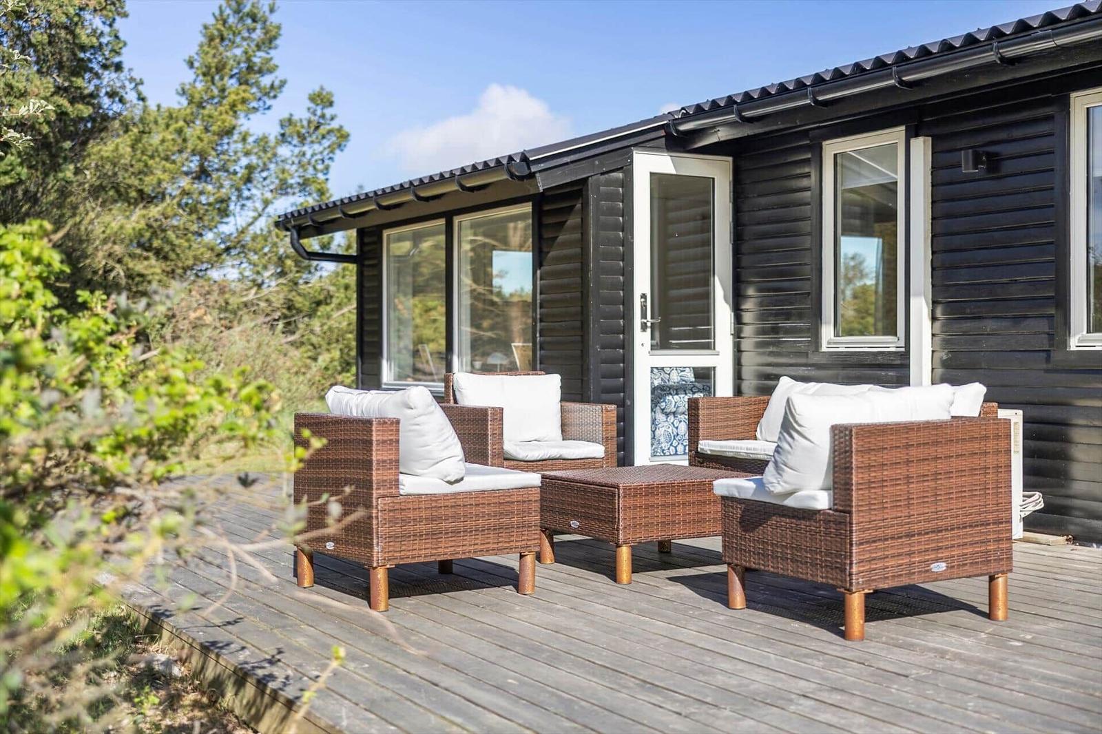 Deck with two chairs and table in front of a house with black siding.