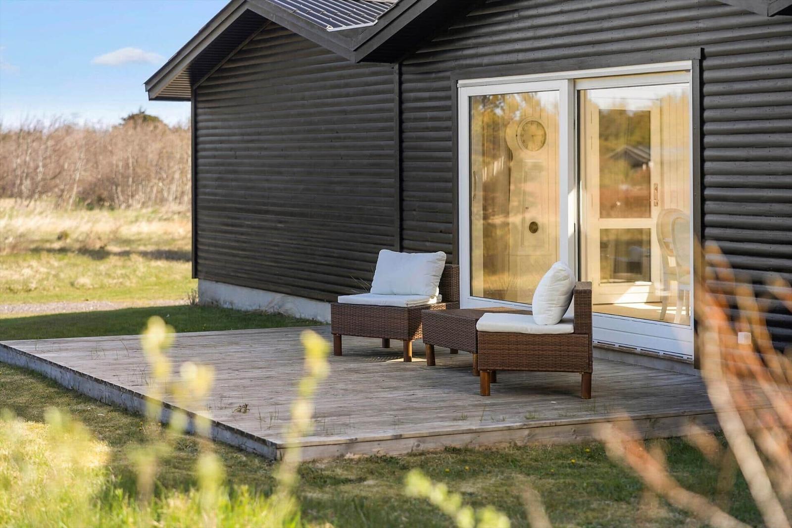 Deck with two seating areas in front of a house with wooden siding and glass door.