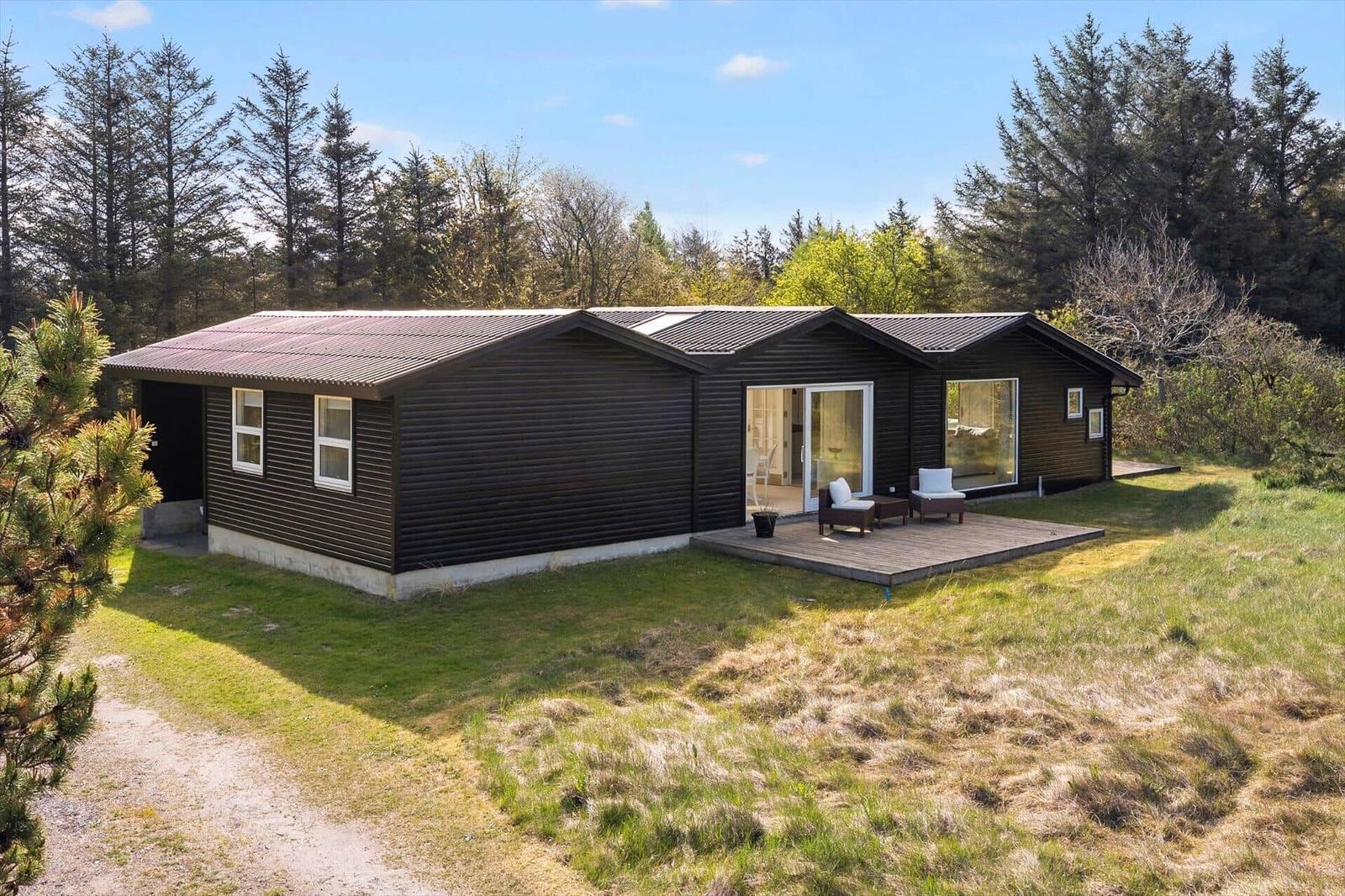 Modern wooden cabin with terrace and garden. Surrounded by trees and grass.