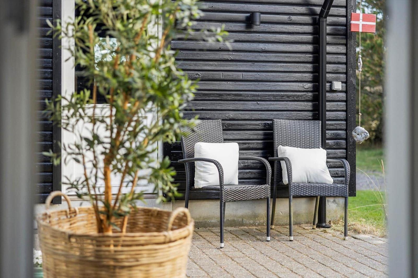 Two chairs with cushions are in front of a wooden house. A planter is in the foreground.