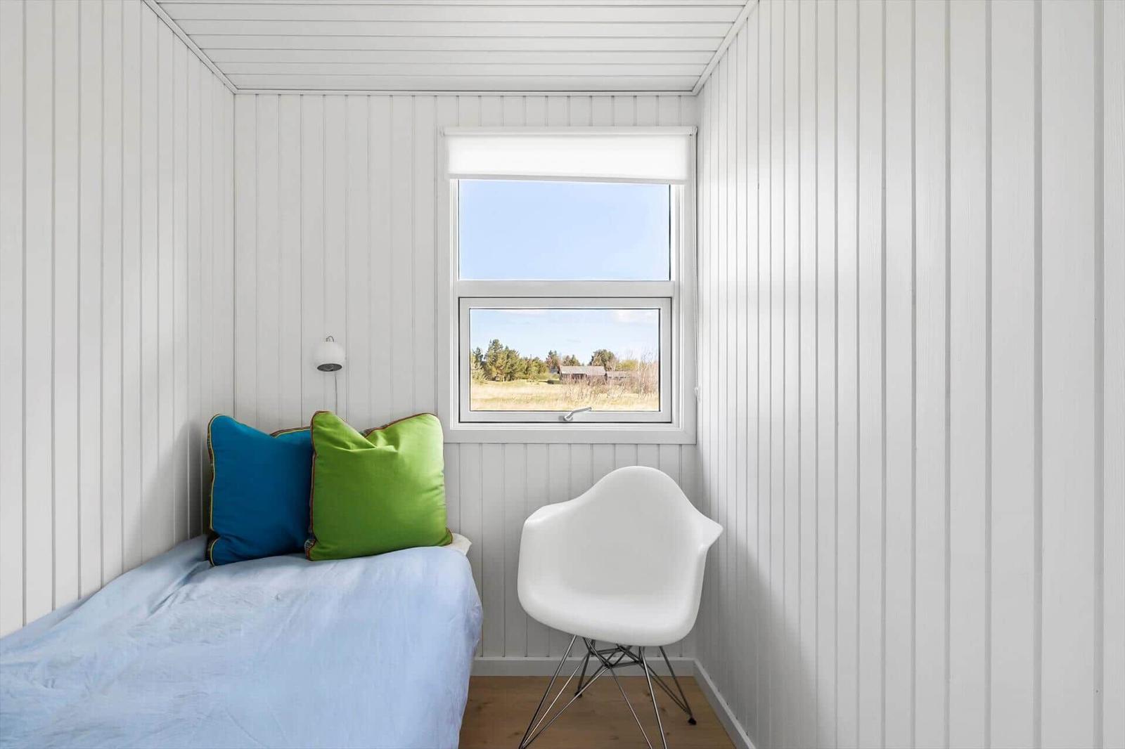 Bedroom with bed, pillows, and chair. Window with view of field and sky.