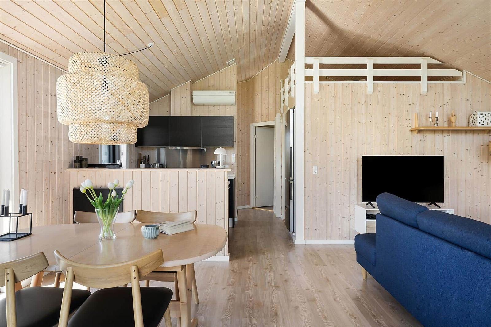 Living area with dining space, kitchen, and sofa under wooden ceiling.