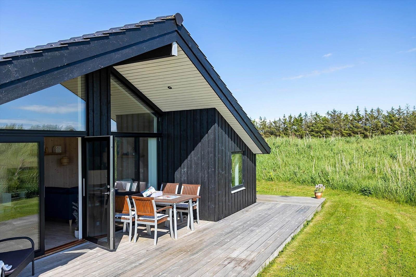 Modern wooden cabin with terrace, garden table, and view of grassland.