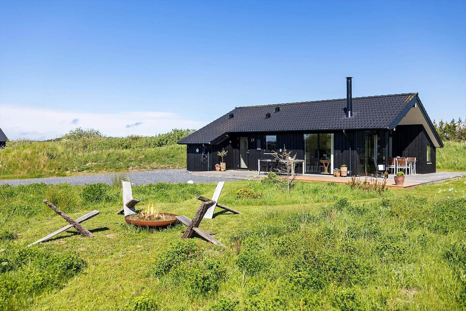 Black holiday home with terrace, fire pit, and garden. Modern design with large window area.