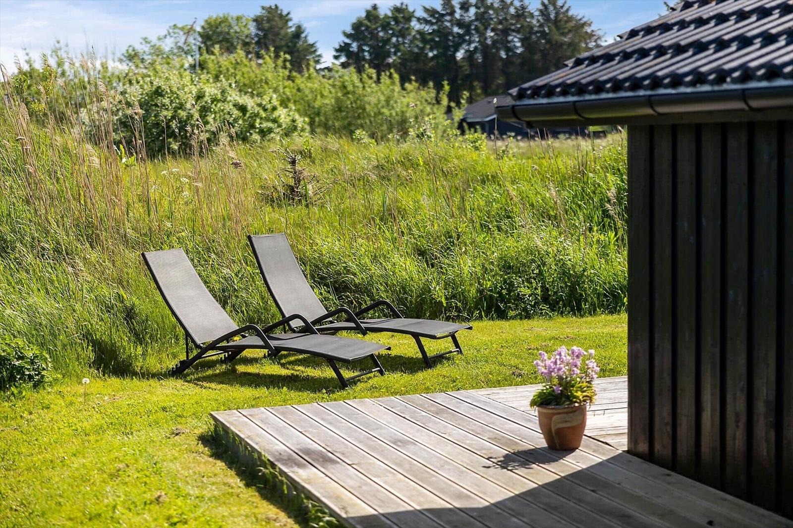 Two lounge chairs on a wooden deck in front of a cabin with grassland in the background.