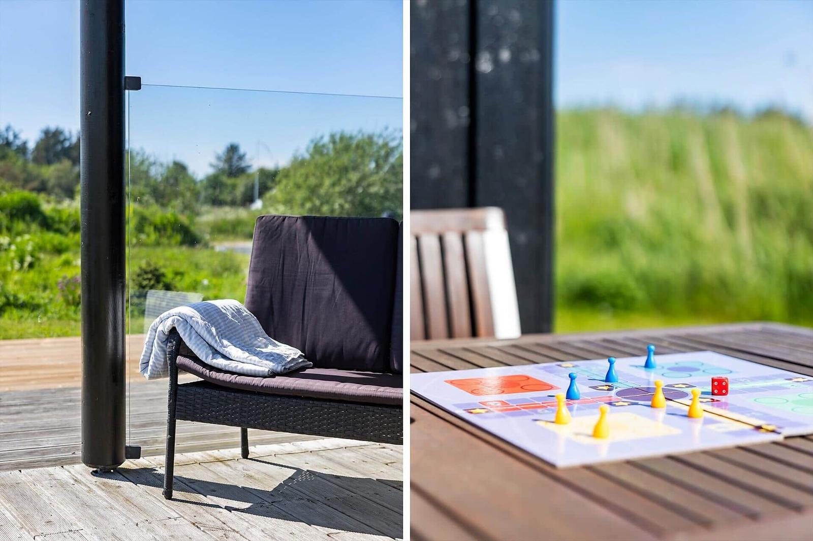 Outdoor area with lounge chair and table with board game. Wooden terrace and green landscape in the background.