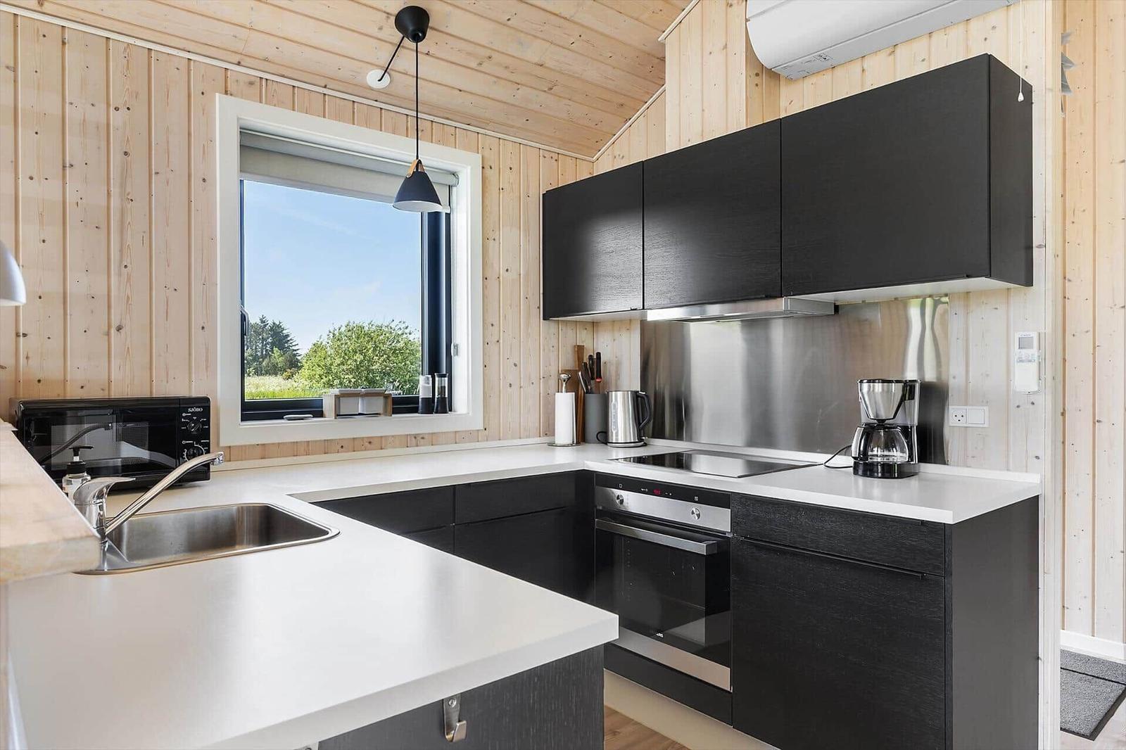 Kitchen with black cabinets, white countertop, and window view of greenery.