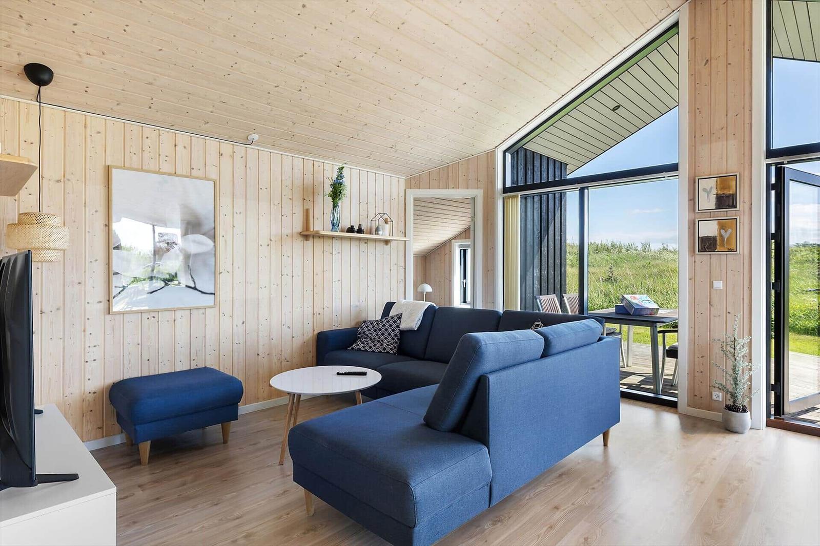 Living room with blue sofa, wooden walls, and large window view of green areas.