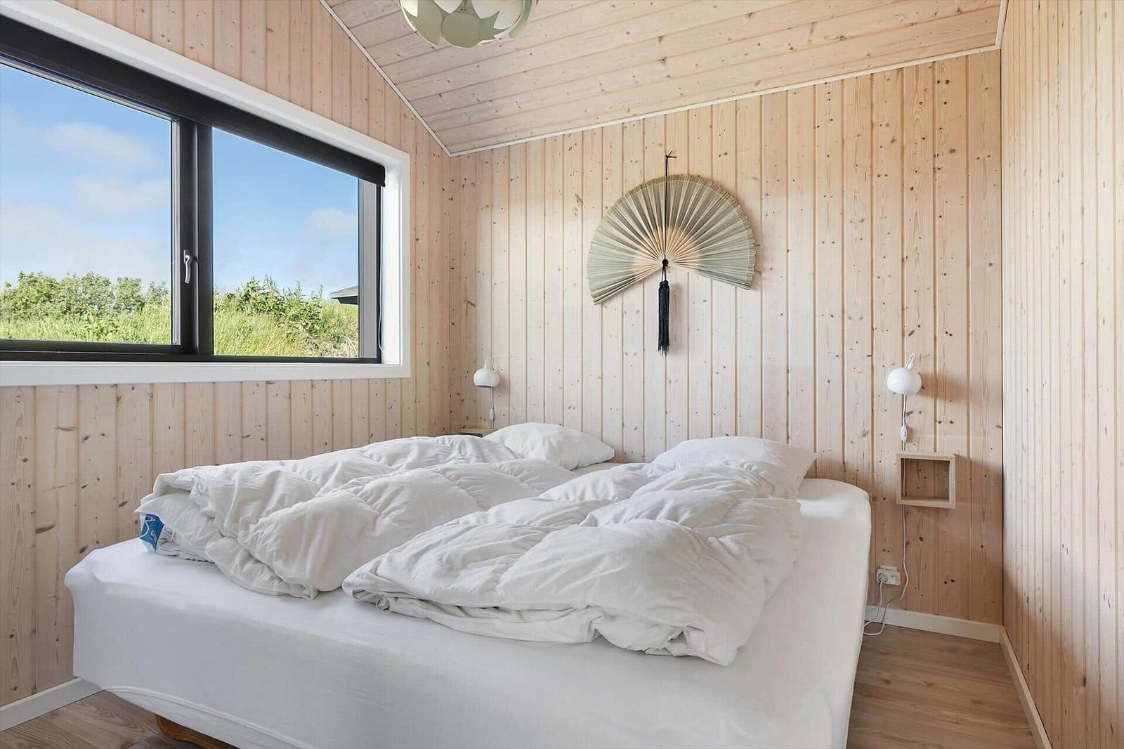Bedroom with wooden walls, large window, and bed with white bedding.