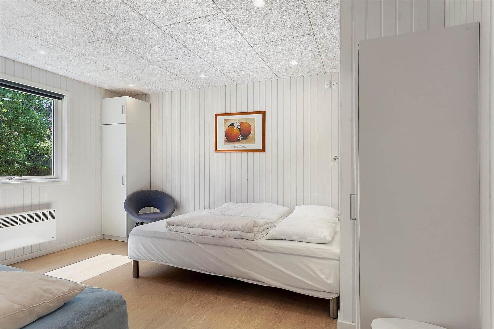 Schlafzimmer mit Bett, Stuhl und Fenster. Wandbild und Kleiderschrank sichtbar.