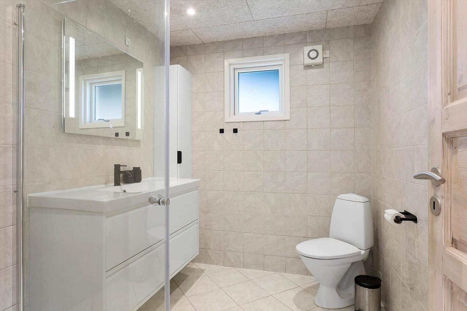 Badezimmer mit Toilette, Waschbecken und Dusche. Fenster und Spiegel sichtbar.