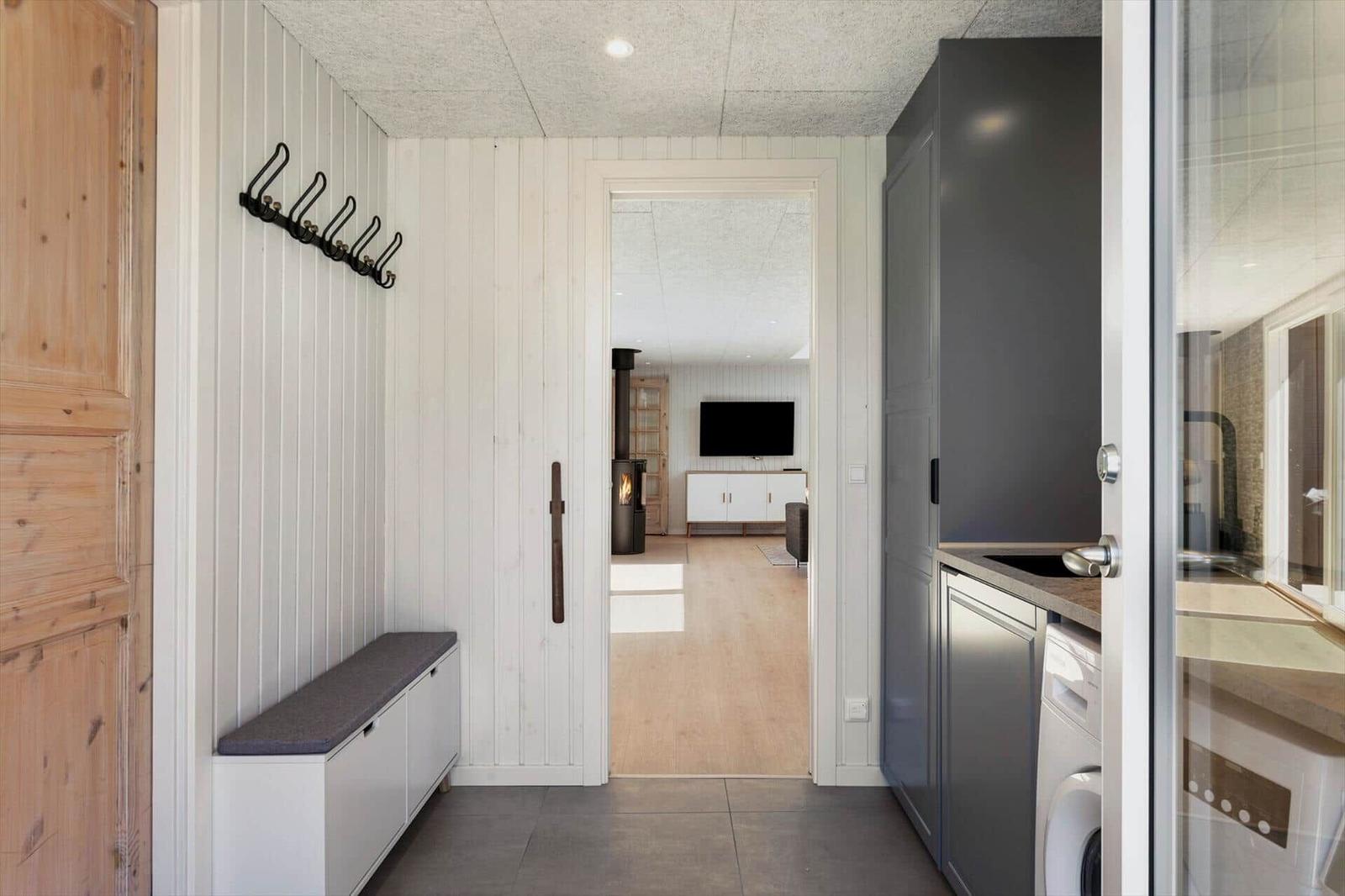 Eingangsbereich mit Garderobe, Sitzbank und Blick in Wohnzimmer mit Kamin und Fernseher.
