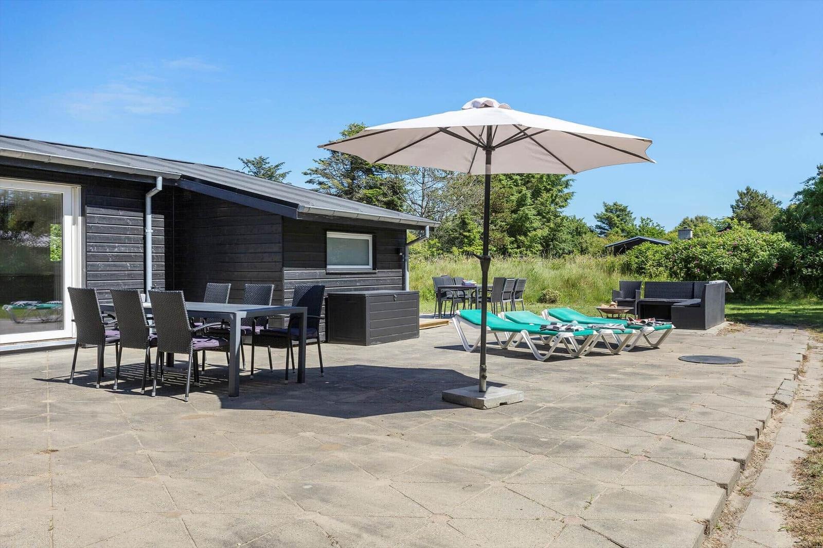 Terrasse mit Tisch, Stühlen, Sonnenschirm und Liegestühlen neben einem Haus.