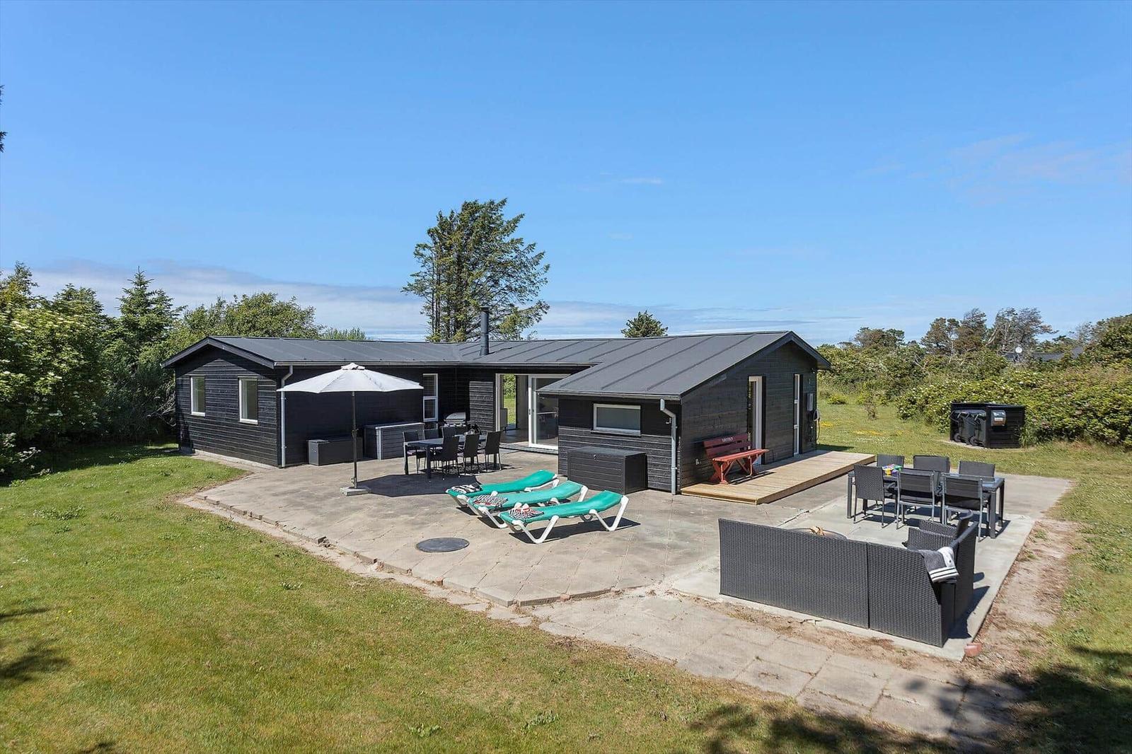 Moderne Holzhütte mit Terrasse, Liegen und Grillplatz im Grünen.