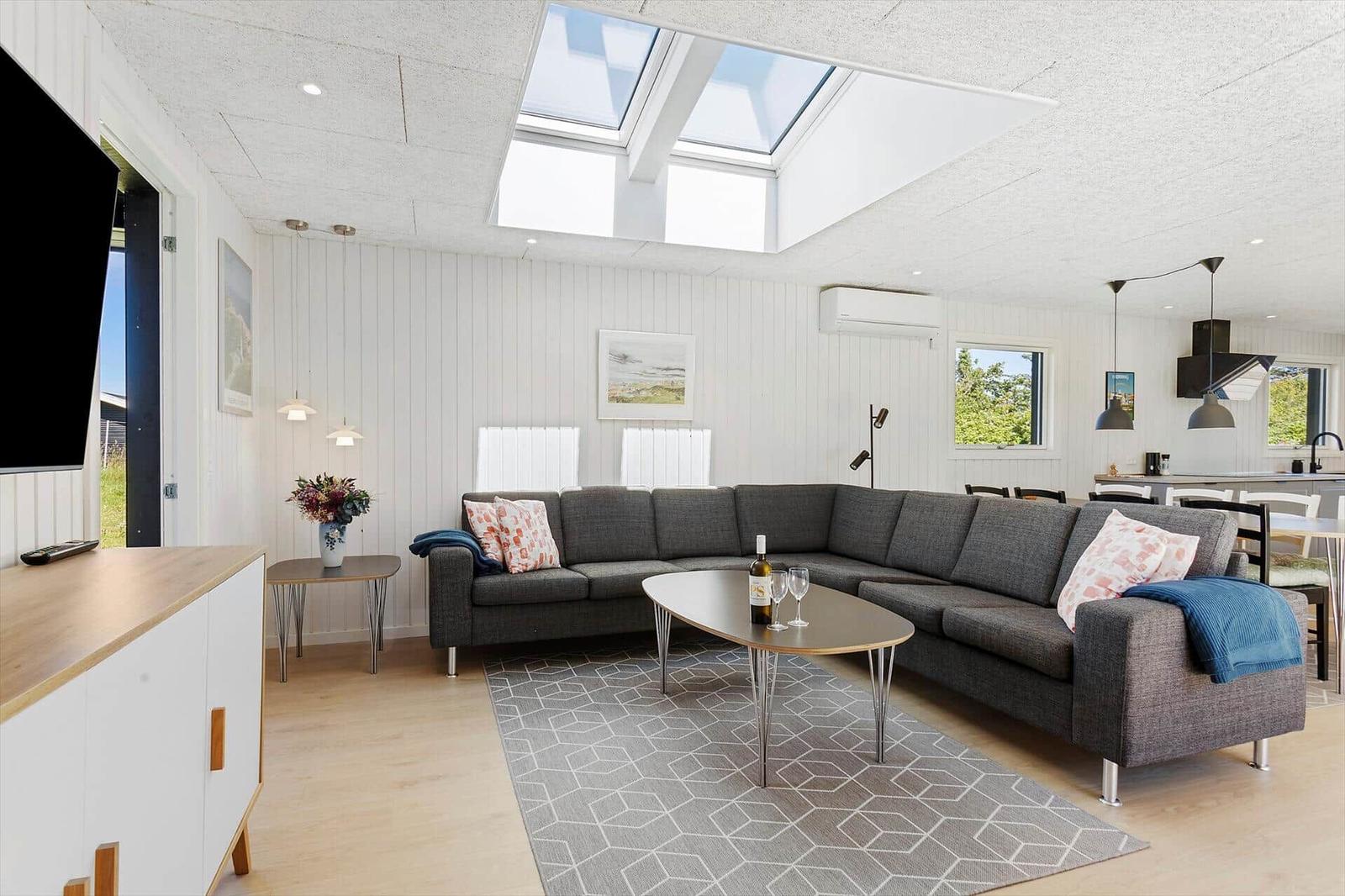 Wohnbereich mit grauem Sofa, ovalen Tisch und Dachfenstern. Küche im Hintergrund.