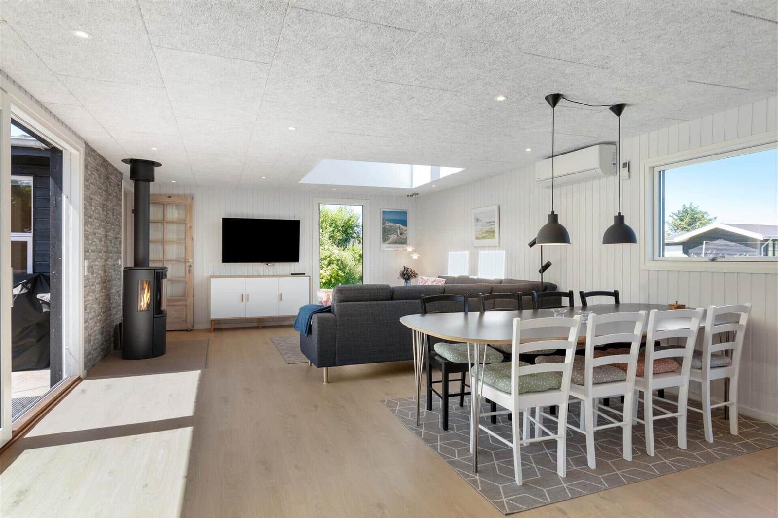 Wohn- und Essbereich mit Esstisch, Sofa und Kaminofen. Große Fenster und Dachfenster.