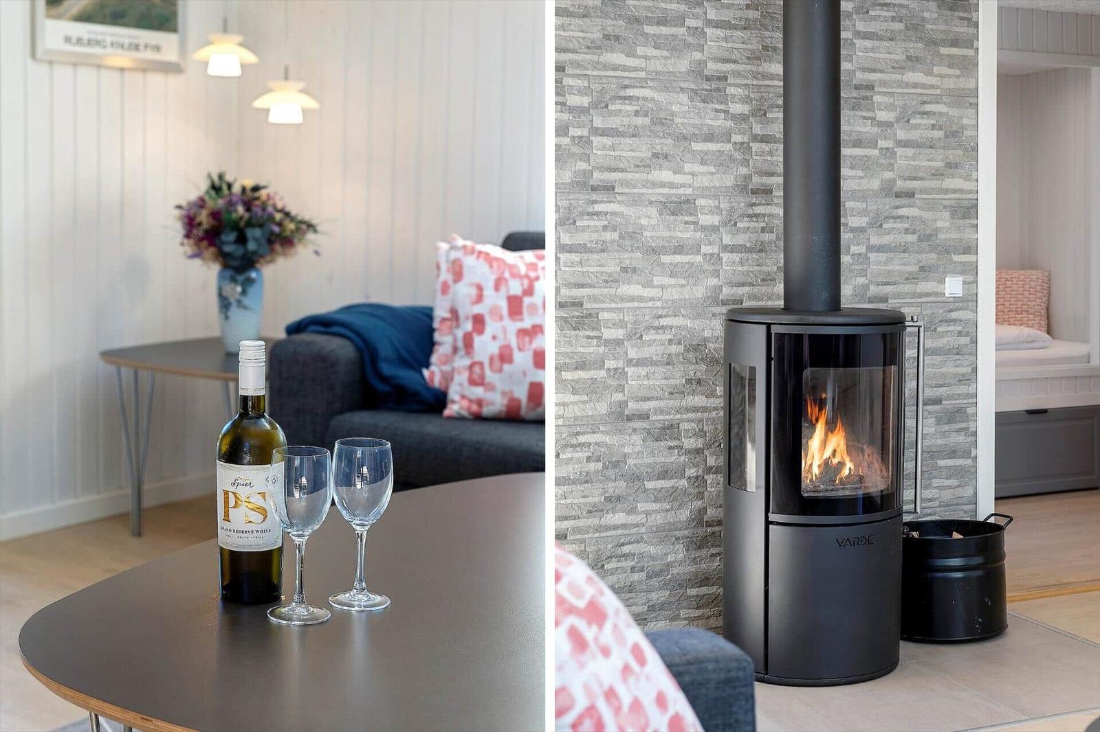 Ein Wohnzimmer mit Sofa, Tisch und Wein. Ein Kaminofen brennt an der Wand.