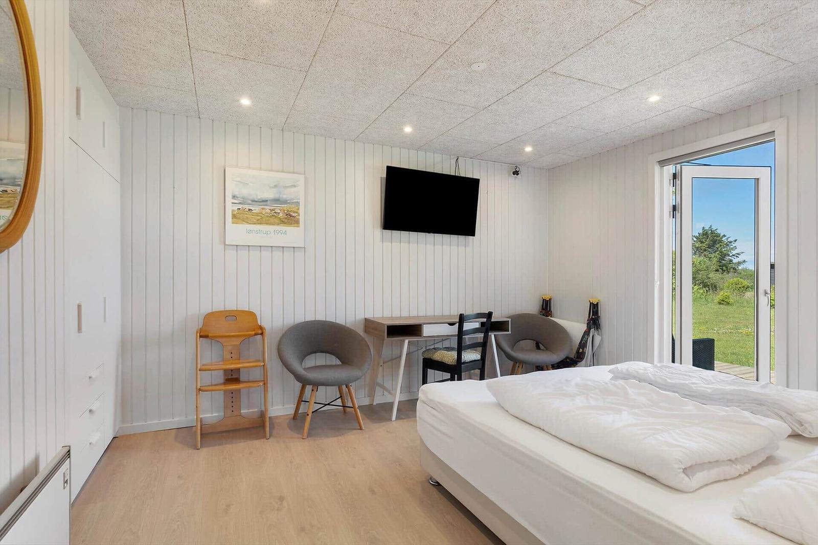 Schlafzimmer mit Bett, Schreibtisch, Stühlen und TV. Tür führt auf einen Außenbereich.