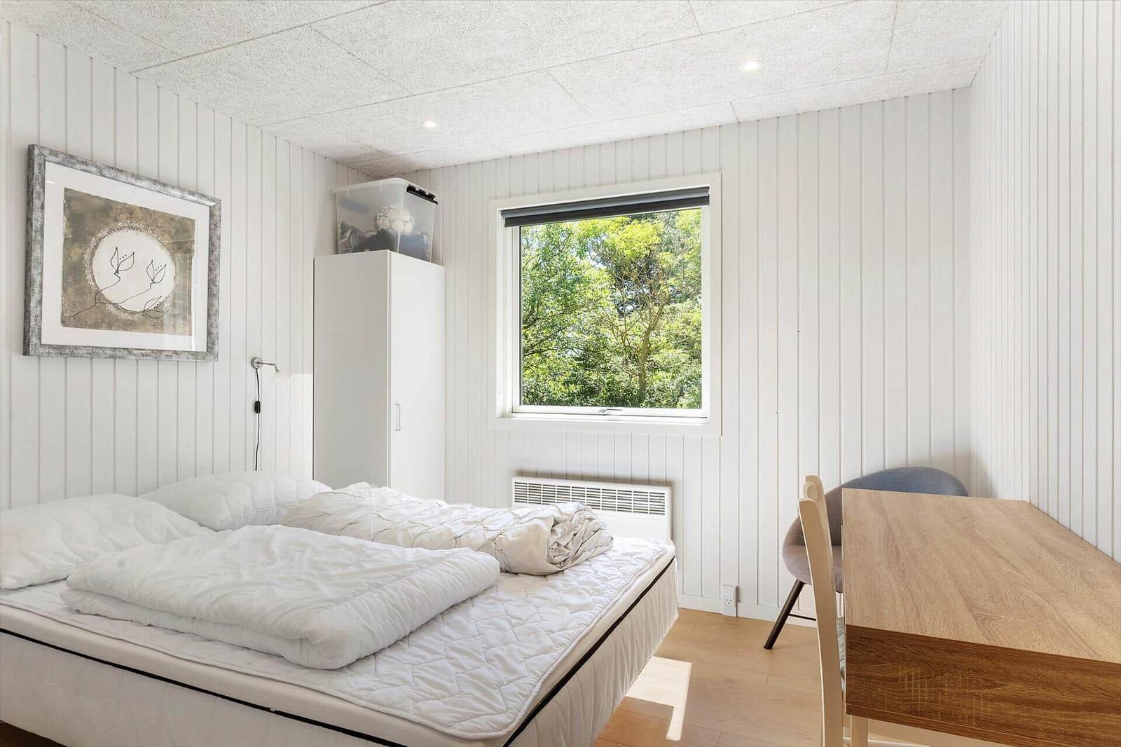 Schlafzimmer mit Bett, Schreibtisch und Fenster mit Blick auf Bäume.