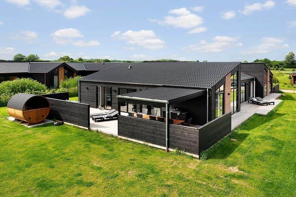 Moderne Villa mit Terrasse, Liegen und Holzsauna auf grünem Grund.