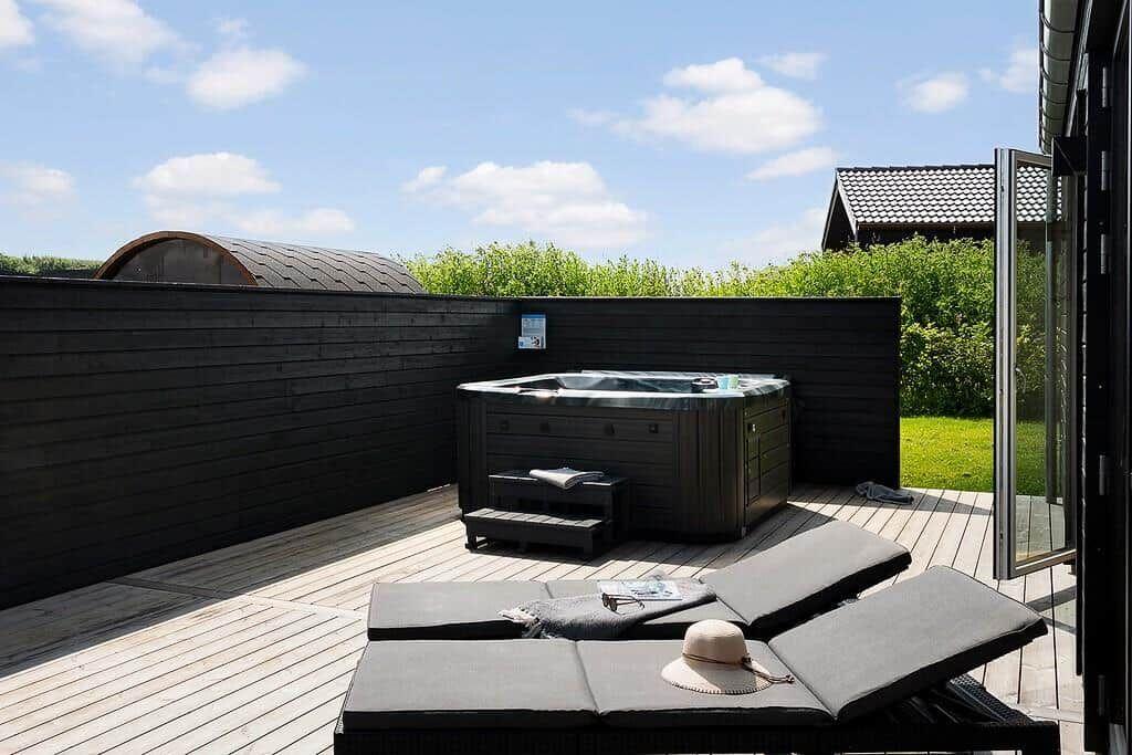 Terrasse mit Whirlpool und Liegen. Schwarze Holzwand und grüner Garten im Hintergrund.