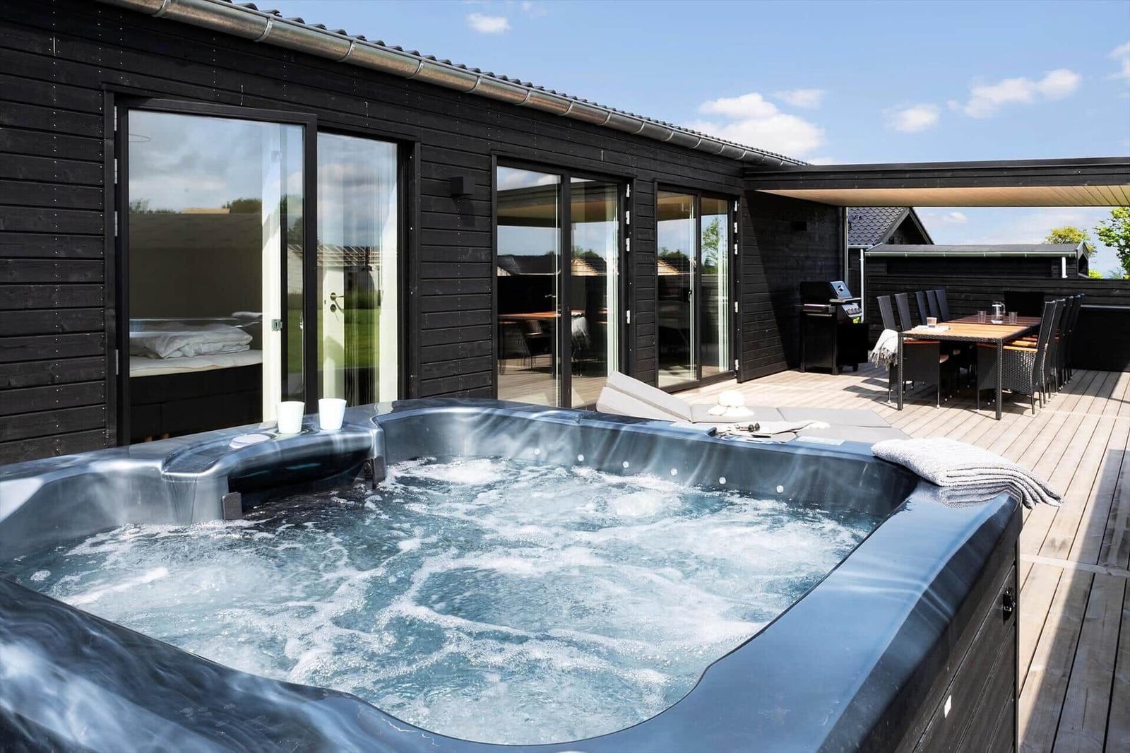 Außenbereich mit Whirlpool, Terrasse und Sitzgruppe. Schwarze Holzfassade und Glastüren.