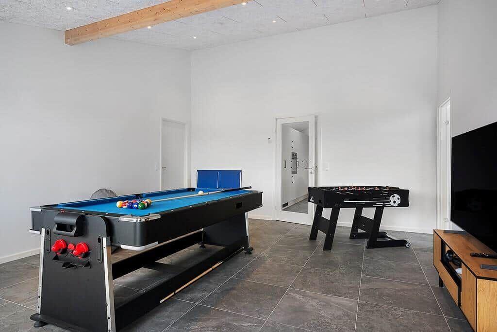 Raum mit Billardtisch und Tischfußball, dunkler Boden, weiße Wände und Fernseher.
