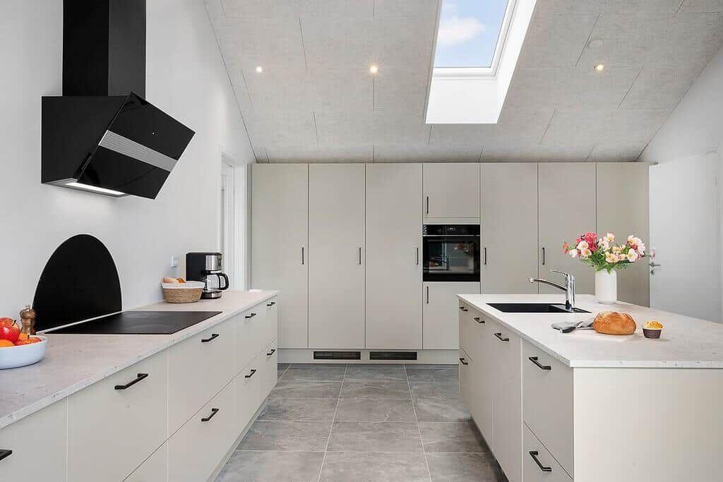 Moderne Küche mit hellen Schränken, Arbeitsplatten und Dachfenster. Einbauküche mit Spüle und Backofen.