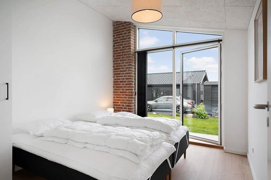Schlafzimmer mit Doppelbett, großem Fenster und Blick auf Garten.