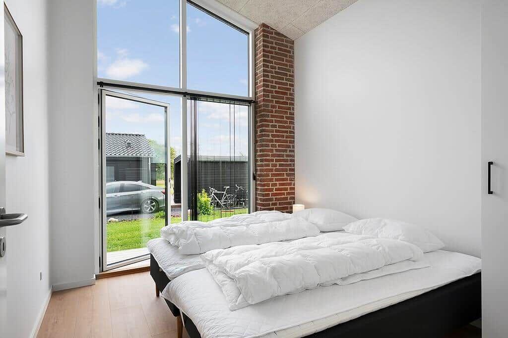 Schlafzimmer mit weißem Bett und großem Fenster zur Außenterrasse.