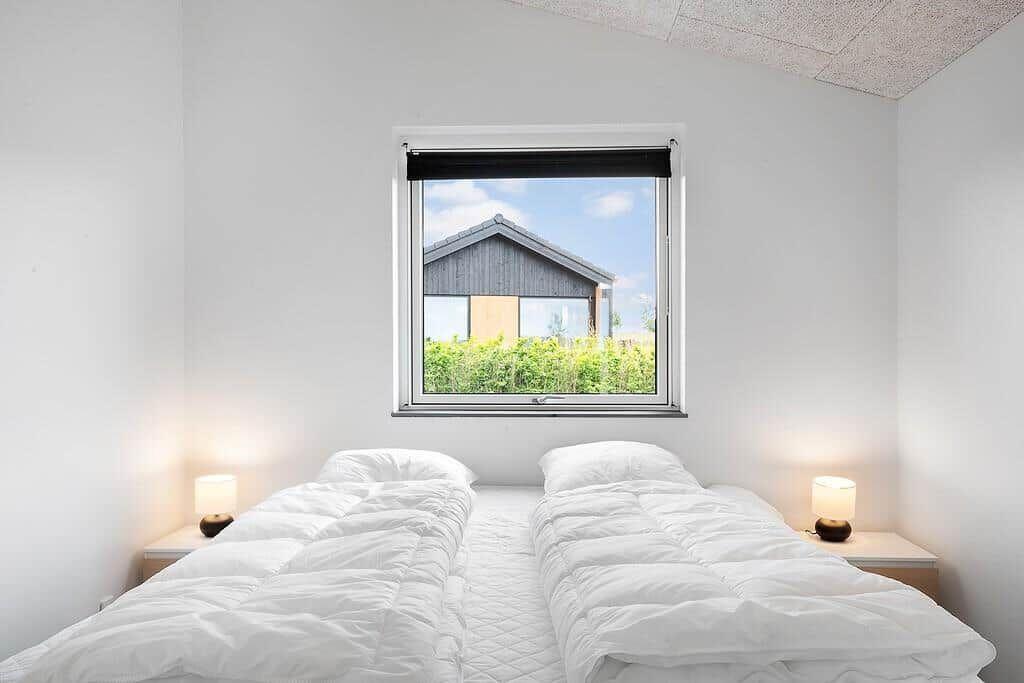 Zwei Betten mit weißen Bettwäschen unter einem Fenster mit Blick auf ein Haus.