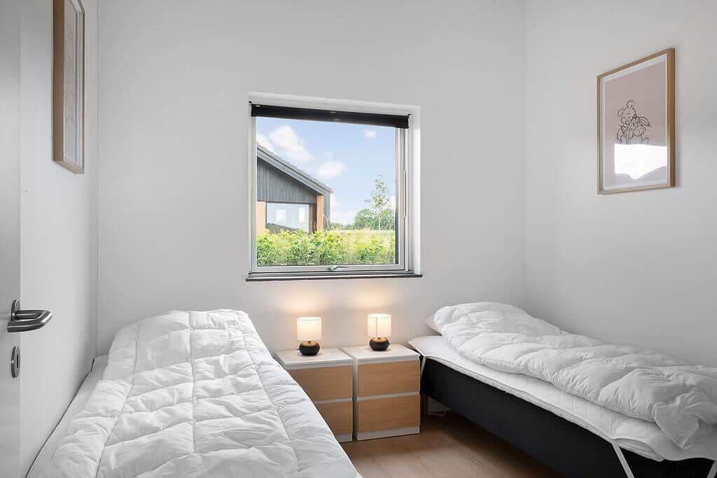 Zwei Betten mit weißen Bettwäschen, Nachttische mit Lampen und ein Fenster mit Blick auf Grün.