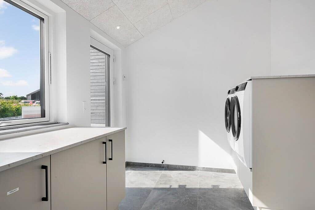 Wohnung mit Waschmaschine und Fenster. Fliesenboden und weiße Wände.