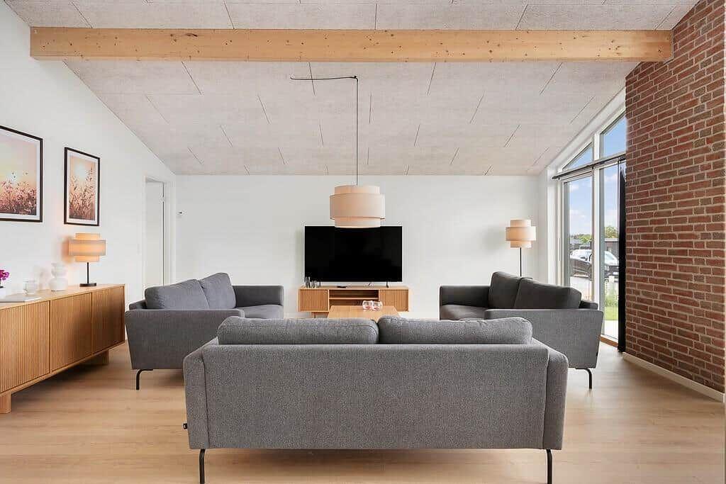 Wohnzimmer mit grauen Sofas, Holzboden und Backsteinwand. Fernseher und Beleuchtung sichtbar.