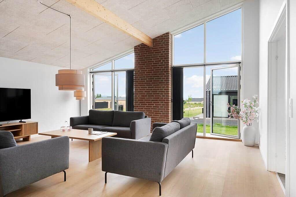 Wohnzimmer mit grauen Sofas, Holzboden und großen Fenstern zur Außensicht.