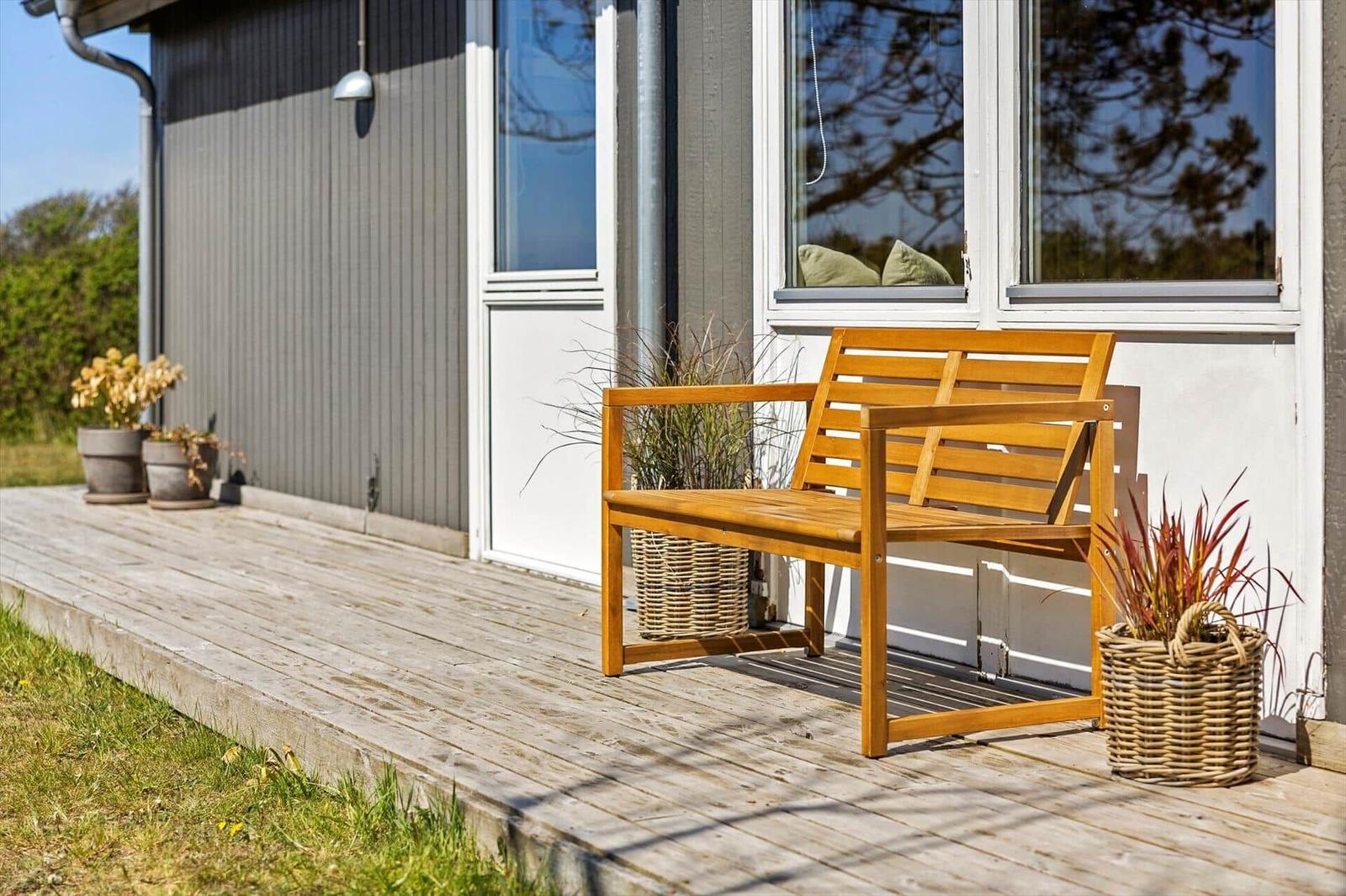 Wooden bench on terrace in front of house with windows and plants in baskets.