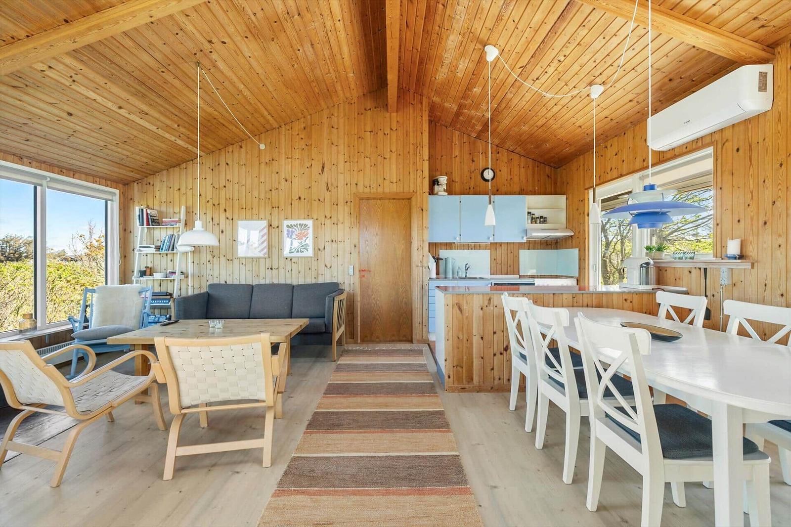Living and dining area with wooden walls, kitchen island, and windows.